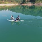 SUP paddle board with electric thruster cruising on a calm lake surrounded by green mountains