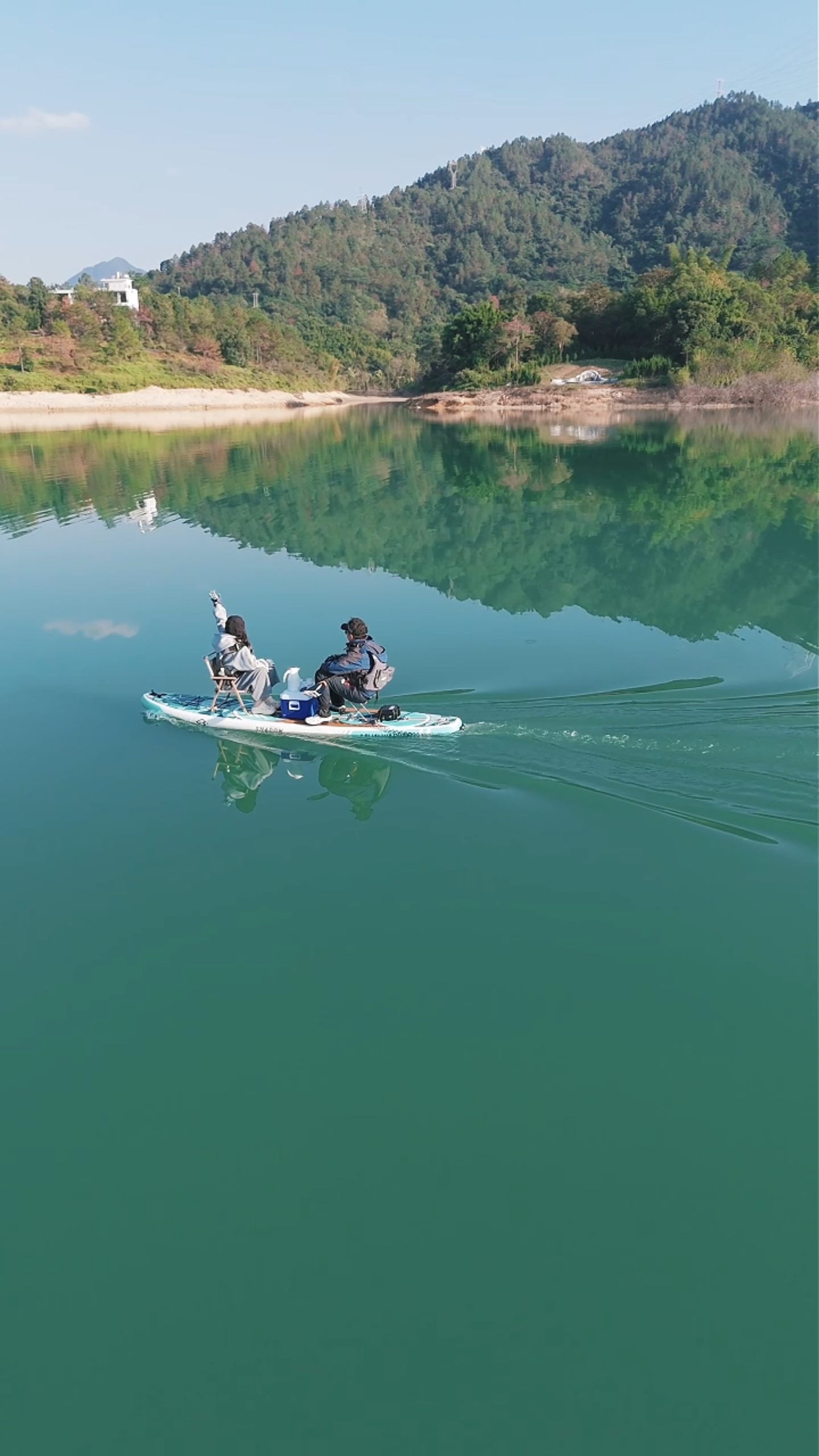 SUP paddle board with electric thruster cruising on a calm lake surrounded by green mountains